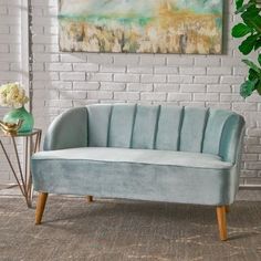 a gray couch sitting in front of a white brick wall next to a vase with flowers