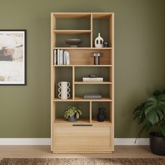 a wooden shelf with books and vases on it in front of a green wall