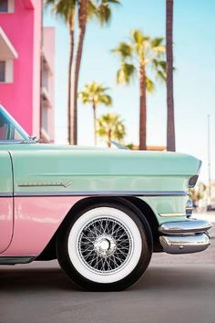 an old pink and mint green car parked in front of a building with palm trees