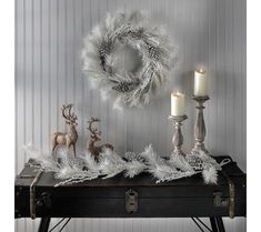 a table topped with two candles and a wreath filled with white feathers on top of it