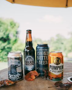 beer bottles and cans sitting on top of a wooden table next to an open umbrella