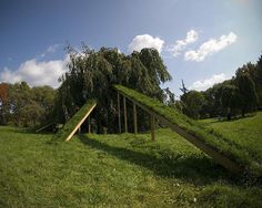 an upside down wooden structure in the middle of a green field with trees and grass