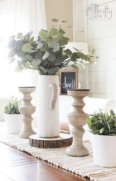 three white vases filled with plants sitting on top of a wooden table in front of a window