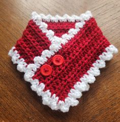 a crocheted red and white sweater with two buttons on the front, sitting on a wooden table