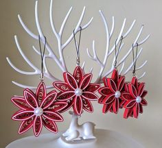 red and white paper flowers are hanging from the branches of a tree with pearls on them