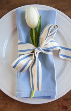 a white tulip sitting on top of a blue and white napkin wrapped in ribbon