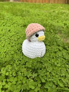 a crocheted duck wearing a pink hat sitting in the middle of clovers