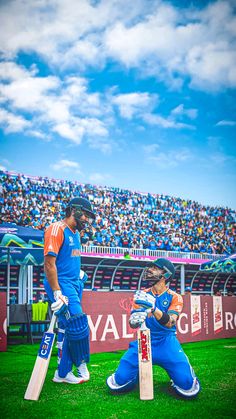 two men in blue and orange uniforms playing cricket on a field with fans watching from the bleachers