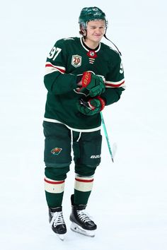 a man in green jersey holding a hockey stick and wearing black gloves with white lettering on it