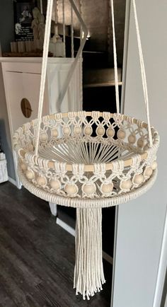 a white hanging basket with tassels and beads on the bottom, in front of a door