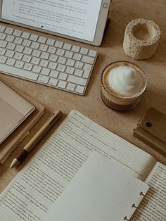 an open notebook sitting on top of a table next to a keyboard and cupcake