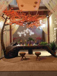 a room decorated with orange and white flowers on the ceiling, two stools under a tree