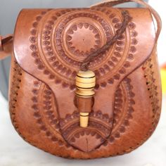 This beautiful sol design leather bag is hand-tooled by our artisan partner Daniel & family at his home work shop in Chiapas, Mexico. Each bag is individually hand-tooled onto quality thick leather, small variations in design and color can occur. Details: Can be worn over the shoulder or cross bodied. Adjustable strap for length- 55” 7 inch L x 8 inch H Wooden closure 100% Pure and Thick Cow Leather. All items are shipped from US Due to the handmade nature and the rawness of the leather, each ba Artisan Shoulder Bag With Leather Lining, Traditional Leather Satchel With Adjustable Strap, Artisan Hand Tooled Shoulder Bag For Daily Use, Artisan Hand-tooled Shoulder Bag For Festivals, Bohemian Hand Tooled Leather Shoulder Bag, Artisan Brown Satchel For Festival, Traditional Shoulder Bag With Leather Lining, Traditional Handmade Leather Satchel, Artisan Hand Tooled Satchel Shoulder Bag