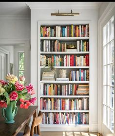 a room with bookshelves full of books and flowers on the table in front of it