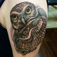 an owl tattoo on the back of a woman's left arm and shoulder, with yellow eyes