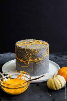 a cake with yellow icing sitting on top of a white plate next to two small pumpkins