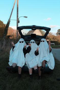 three people in white robes sitting on the hood of a car with their hands up