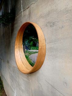 a circular mirror mounted to the side of a wall next to a tree and grass