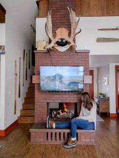 a woman sitting in front of a fire place with a deer head mounted on the wall