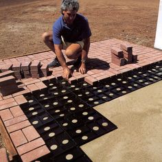 a man kneeling down on top of a red brick floor next to blocks and circles