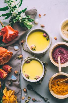 bowls filled with different colored powders next to flowers and spoons on a table