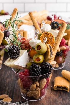 an assortment of snacks in small cups on a wooden table with crackers and nuts