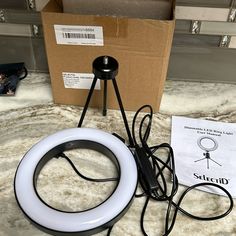 a white ring light sitting on top of a table next to a cardboard box and some wires