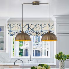 two lights hanging over a kitchen island in front of a window with blue and white curtains