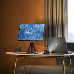 a laptop computer sitting on top of a wooden desk next to a window with curtains