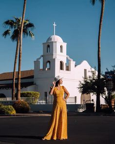 a woman standing in front of a church wearing a long yellow dress and white hat