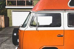 an orange and white vw bus parked in front of a house with two garage doors