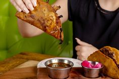 a woman is eating a piece of pizza on a plate with dipping sauces next to her