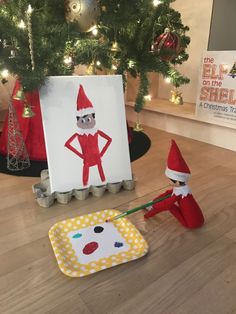 an elf painting on the floor next to a christmas tree