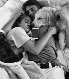 a man and woman laying in bed next to a dog with an electronic device on their lap