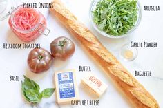 ingredients to make an italian salad laid out on a white counter top, including tomatoes, cheese, basil, and bread