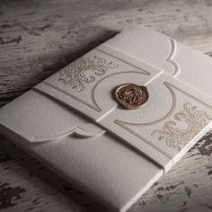 a white and gold wedding card with a wax stamp on it's front pocket