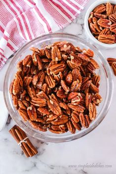 two bowls filled with pecans on top of a marble counter next to cinnamon sticks