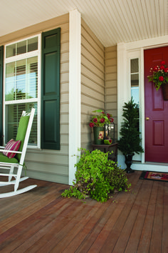 a porch with rocking chairs and potted plants on the front steps, next to a red door