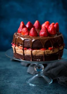 a chocolate cake topped with strawberries on top of a glass platter next to a blue background