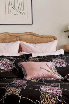 a bed with black and pink comforter, pillows and pictures on the wall above it