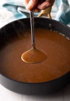 a person holding a spoon over a pan filled with food