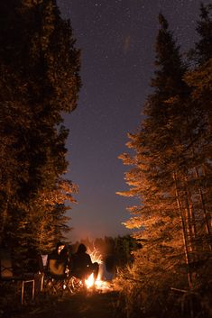 two people sitting around a campfire at night with the stars in the sky above