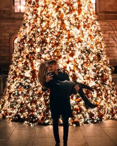 a man holding a woman in front of a christmas tree