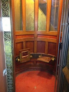 an ornate wooden door is opened to reveal a red carpeted area with metal bars on either side