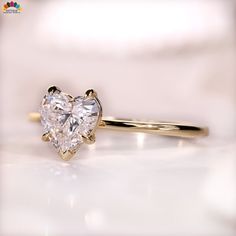 a heart shaped diamond ring sitting on top of a white surface