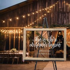 an easel with a wedding sign on it in front of a barn at night