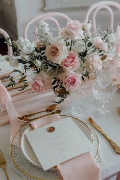 a table set with pink and white flowers in vases, gold place settings and napkins