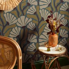 a vase with flowers on a table next to a wicker chair and wallpaper