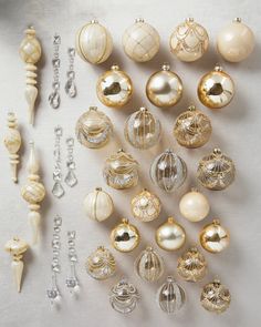 an assortment of christmas ornaments are displayed on a white tablecloth with silver and gold accents