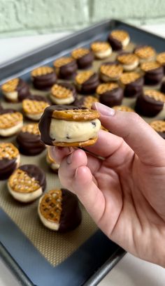 a hand holding a cookie with chocolate and pretzel toppings in the background